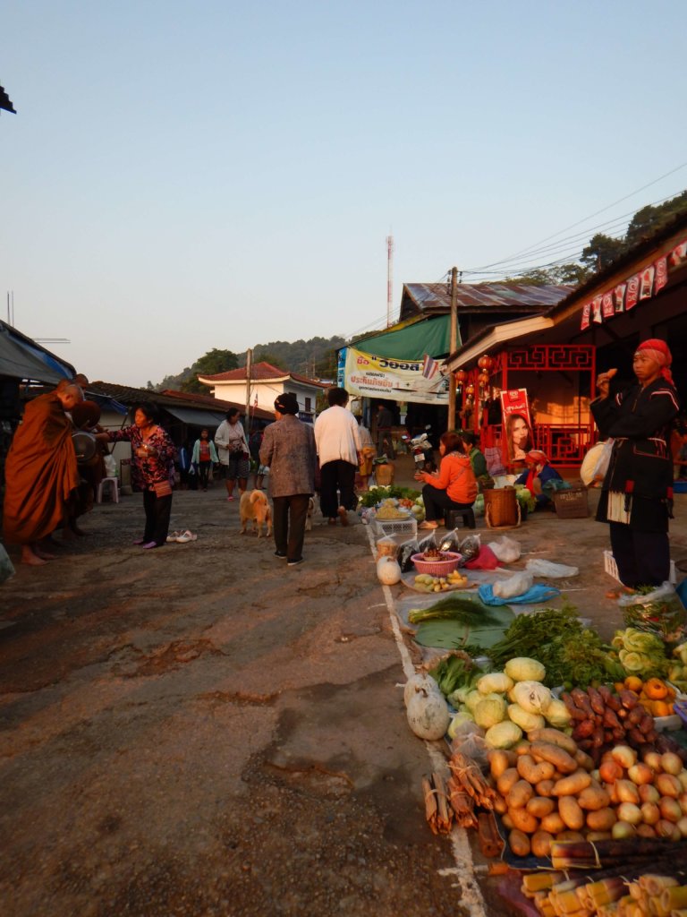 Mae Salong in Northern Thailand a morning market with a monk receiving alms from a woman and sellers with vegetables and fruits