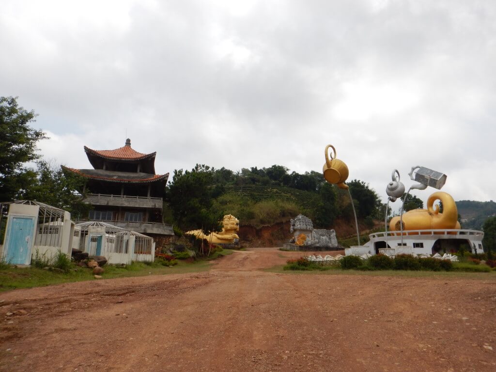 Mae Salong in Northern Thailand an abandoned hotel with large tea pot statues, a pagoda-like building, and two large lion statues at the entrance. 
