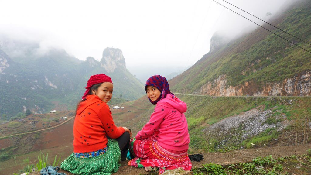 20 Tips from a Local for Planning a Trip to Vietnam. Two girls in bright clothing face the camera with green hills and mountains behind them. 